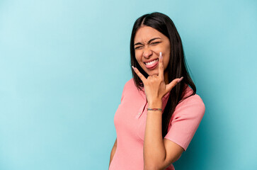 Young hispanic woman isolated on blue background showing rock gesture with fingers