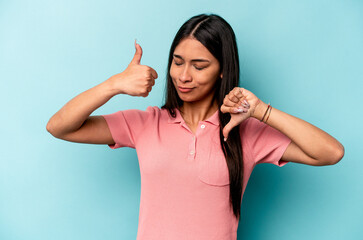 Young hispanic woman isolated on blue background showing thumbs up and thumbs down, difficult choose concept