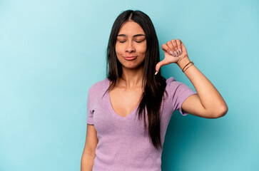 Young hispanic woman isolated on blue background showing a dislike gesture, thumbs down....