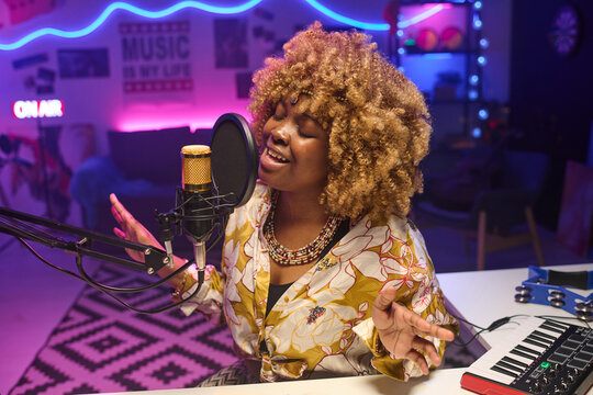 High angle medium shot of young African American woman sitting at desk in home studio recording rnb song
