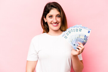 Young caucasian woman holding banknotes isolated on pink background happy, smiling and cheerful.