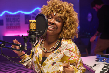 Horizontal shot of young African American woman wearing stylish outfit recording song in amateur...