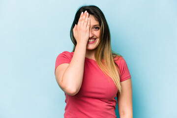 Young caucasian woman isolated on blue background having fun covering half of face with palm.