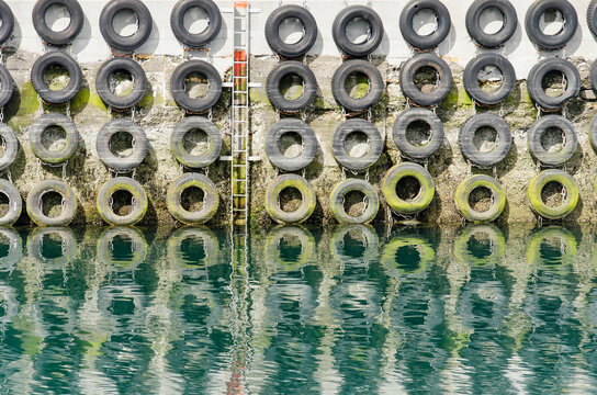 Old car tyres for protestion of the hull of mooring ships, and an emergency ladder attached to a rough concrete wall in a small harbou rin Iceland
