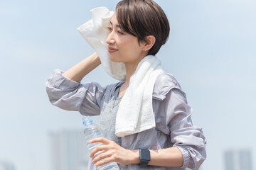 青空、公園でランニング・ウォーキング中にタオルで汗を拭く爽やかな日本人女性 - obrazy, fototapety, plakaty