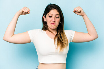 Fototapeta premium Young caucasian woman isolated on blue background showing strength gesture with arms, symbol of feminine power