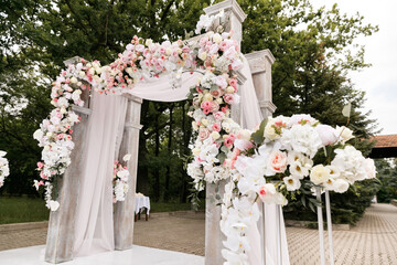 Wedding ceremony decorated with flowers and fabrics in light colors on the arch
