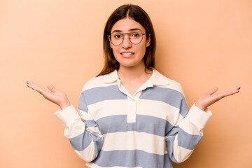 Young hispanic woman isolated on beige background confused and doubtful shrugging shoulders to hold...