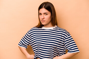Young hispanic woman isolated on beige background frowning face in displeasure, keeps arms folded.
