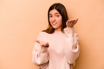 Young hispanic woman isolated on beige background makes scale with arms, feels happy and confident.