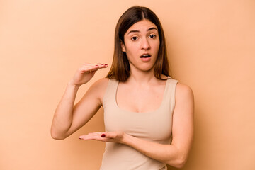 Obraz premium Young hispanic woman isolated on beige background holding something with both hands, product presentation.
