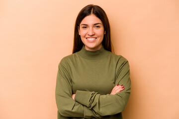 Young hispanic woman isolated on beige background who feels confident, crossing arms with determination.