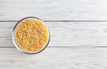 Uncooked vermicelli pasta in glass bowl on white wooden table