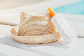 summer straw hat and sunblock on white sun lounger near pool, vacation concept - Powered by Adobe