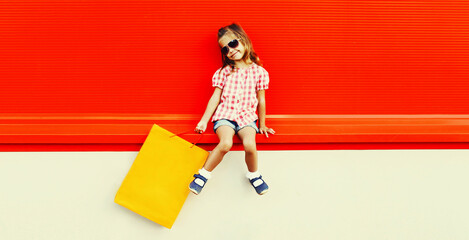 Little girl child with shopping bags in the city on red background