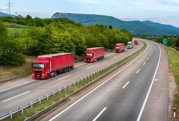 Fototapeta na wymiar Series of red Trucks and one white truck on highway, cargo transportation concept in springtime - freight service