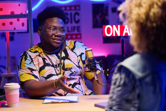 Young African American Male Influencer Sitting At Desk In Front Of His Female Co-worker Sharing Ideas During Coffee Break