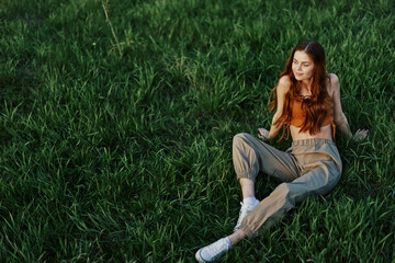 A girl sits on the grass in the park and enjoys the beautiful view of the summer sunset