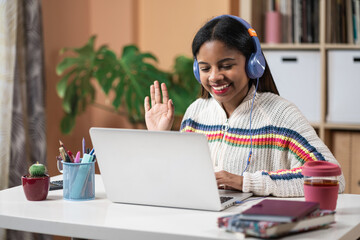 African Latin American girl student waving hand during video call sitting at home . Online Education