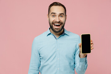 Young amazed man 20s in classic blue shirt hold in hand use mobile cell phone with blank screen workspace area isolated on plain pastel light pink background studio portrait. People lifestyle concept.