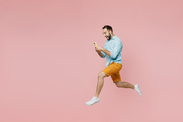Fototapeta na wymiar Full body side view fun young man 20s wearing classic blue shirt hold use mobile cell phone jump high run fast isolated on plain pastel light pink background studio portrait. People lifestyle concept.