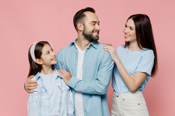 Young happy smiling cool parents mom dad with child kid daughter teen girl in blue clothes look to each other isolated on plain pastel light pink background Family day parenthood childhood concept.