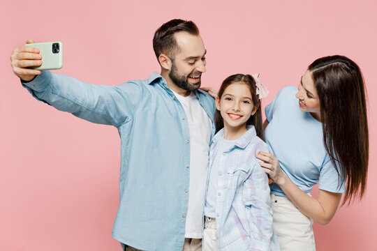 Young smiling parents mom dad with child kid daughter teen girl in blue clothes do selfie mobile cell phone shot post photo social network isolated on plain pastel pink background. Family day concept.