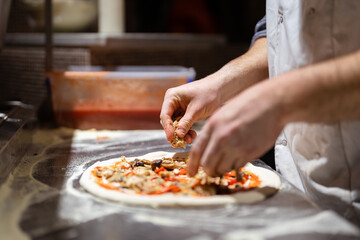 Pizza making process. Male chef hands making authentic pizza in the pizzeria kitchen. - obrazy, fototapety, plakaty