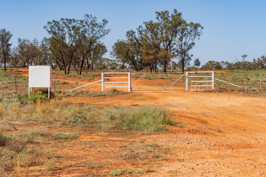 A red dirt drive going through a white gate with a mailbox adjacent