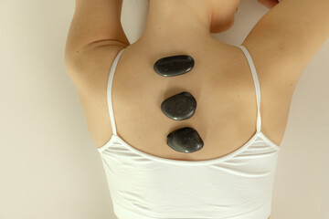 Cropped image of female back with stones isolated over grey studio background. Spa, massage concept