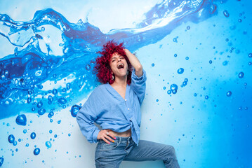portrait of a smiling young latin woman with red afro hair posing on a blue background with blue drops