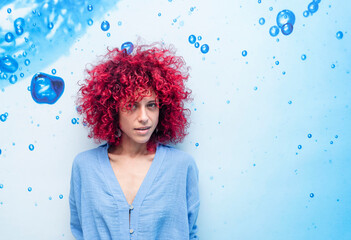 portrait of a smiling young latin woman with red afro hair on a blue background with blue drops