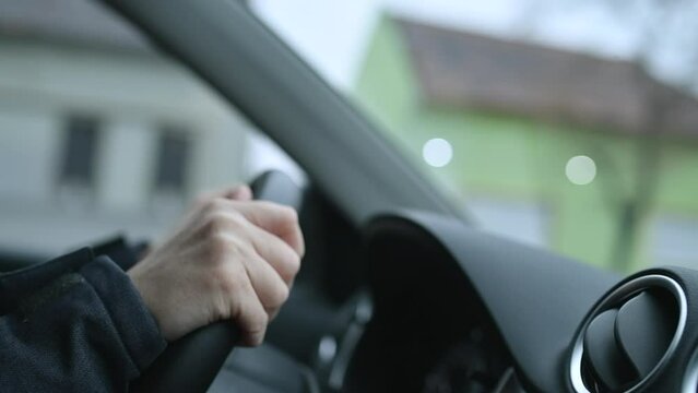 Slow motion closeup shot of female hands gripping automobile steering wheel while driving through town street