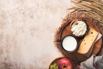 Fototapeta na wymiar Happy Shavuot. Background for Shavuot traditional religious Jewish celebration. Milk and cheese, ripe wheat and fruits. Dairy products over old light brown wall background. Shavuot concept. Top view.