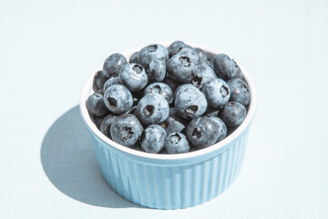 Berries of blueberry in blue bowl on light background, healthy summer food