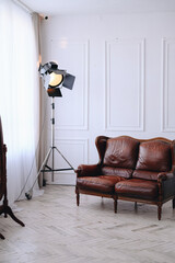 Vertical photo of an interior photo studio with a large loft spotlight and a leather sofa.