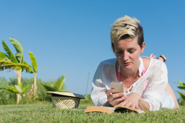 Woman lying and reading her favorite book on a meadow covered with fresh green grass on a sunny summer or spring day.