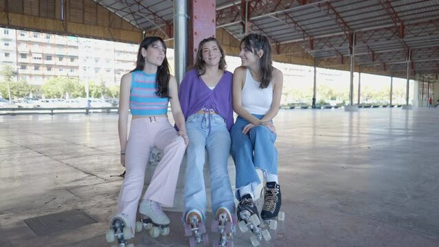 Three girls wearing roller skates sit and talk and laugh, handheld