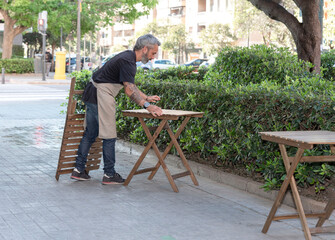 a young waiter setting up the terrace of his bar or cafeteria