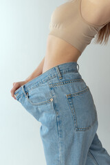 Cropped image of slender woman wearing giant jeans isolated over grey studio background. Weight-loss, dieting concept