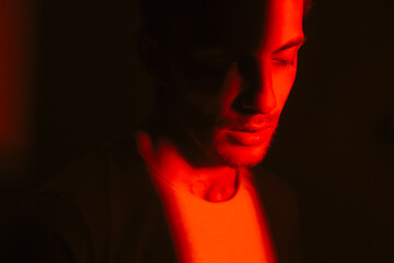 Side view portrait of caucasian young man in a dark with red light.