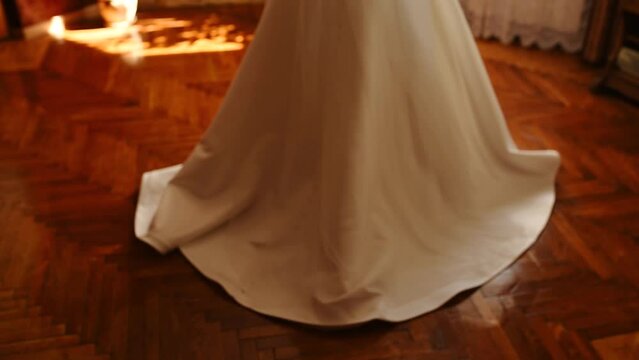bride in white silk wedding dress and long veil moves away from camera. wedding clothes fashionable stylish skirt, hem dress on background wooden brown textured parquet floor.