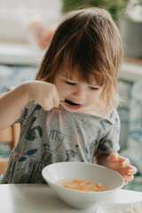 a little girl is sitting at the kitchen table eating soup