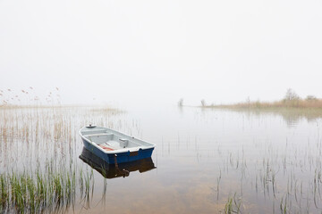 Small fishing boat anchored in a forest lake. Fog, rain. Reflections on water. Transportation,...