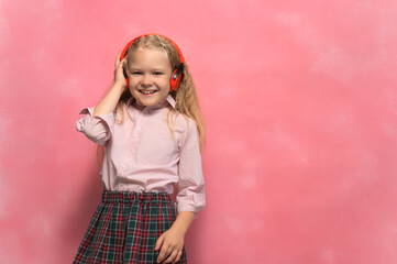Obraz na płótnie Canvas little girl listens to music in wireless headphones. Pink background.