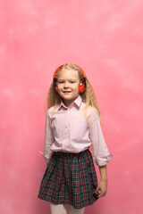 little girl listens to music in wireless headphones. Pink background.