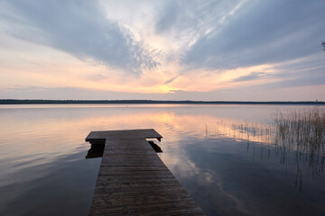 Busnieku lake at sunset. Ventspils, Latvia. Wooden pier. Soft sunlight, glowing clouds, symmetry...