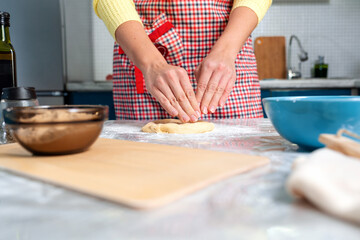 Obraz na płótnie Canvas A woman in an apron kneads dough. Close - look up your hands and dough. The concept of cooking homemade food and slow food