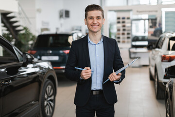 Portrait of positive young auto insurance agent posing in automobile dealership center