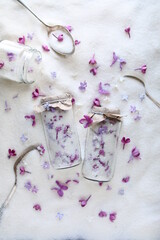 Fototapeta na wymiar Sugar with lilacs in small glass jars on scattered sugar. Edible flowers in cooking and confectionery. Seasonal spring preparations. Lilacs of different varieties.